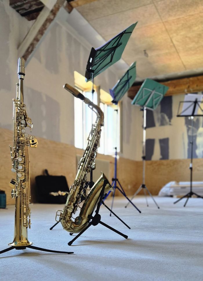 Soprano and alto saxophones with music stands in an empty rehearsal space, ready for practice.